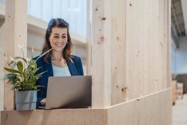 Lächelnde Geschäftsfrau mit Laptop in der Industrie - JOSEF22975