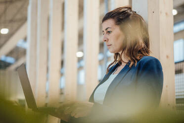 Focused businesswoman working on laptop at industry - JOSEF22976