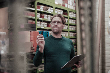 Businessman with clipboard standing in workshop - JOSEF22988