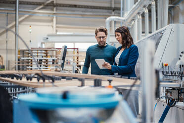 Businesswoman discussing with colleague over tablet computer in industry - JOSEF23030