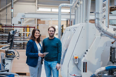 Smiling business colleagues standing machinery in industry - JOSEF23033