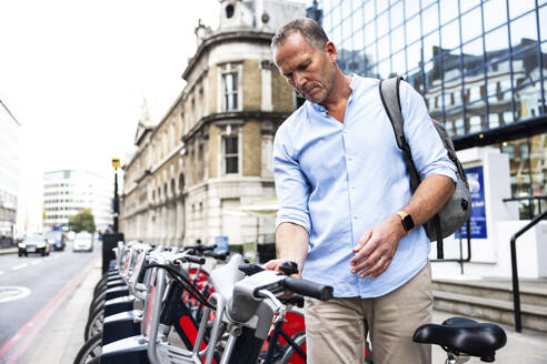 Mature businessman renting electric bicycle with smart phone at street - WPEF08009