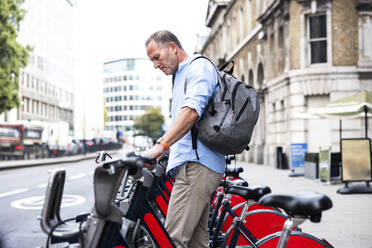 Businessman standing near electric bicycle at street - WPEF08010