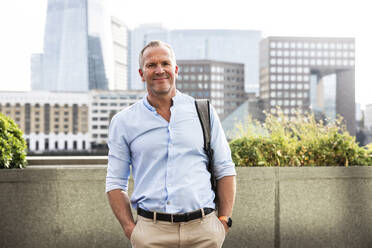 Smiling businessman standing with hands in pockets at London, UK - WPEF08019