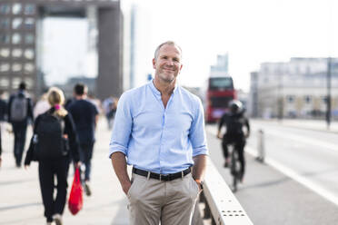 Smiling businessman standing with hands in pockets on footpath at London, UK - WPEF08029