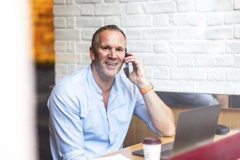 Glücklicher Geschäftsmann, der in einem Café mit seinem Smartphone telefoniert - WPEF08033