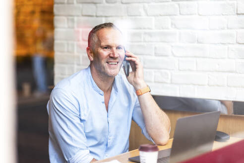 Lächelnder Geschäftsmann, der in einem Café mit seinem Smartphone telefoniert - WPEF08034