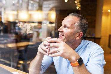 Happy businessman holding coffee cup at cafe - WPEF08039