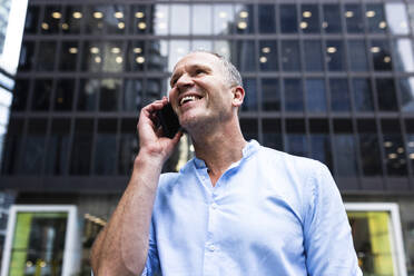 Happy businessman talking on smart phone in front of building - WPEF08044