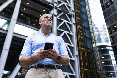 Geschäftsmann mit Smartphone vor einem Bürogebäude - WPEF08047