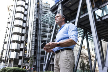 Geschäftsmann hält Smartphone in der Nähe eines Bürogebäudes - WPEF08048