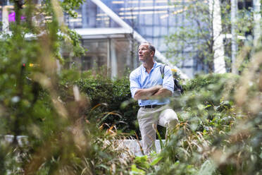 Businessman with arms crossed standing at office park - WPEF08053