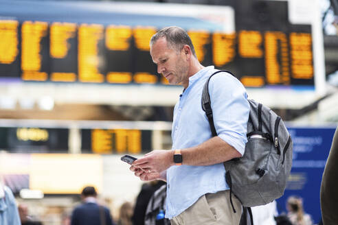 Geschäftsmann mit Rucksack und Smartphone am Bahnhof - WPEF08060