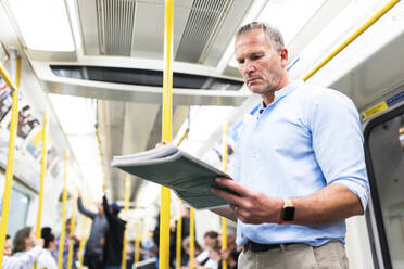 Mature businessman reading newspaper on train - WPEF08066