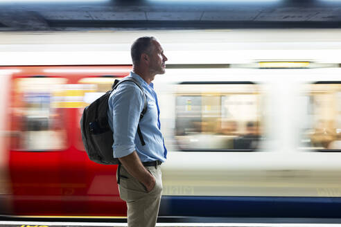 Älterer Geschäftsmann mit der Hand in der Tasche auf dem Bahnsteig stehend - WPEF08068