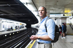 Businessman holding smart phone and waiting for train on platform - WPEF08073