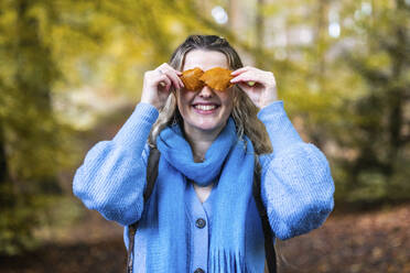 Glückliche Frau bedeckt Augen mit Blättern im Wald - WPEF08080