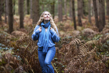 Lächelnde blonde Frau, die in der Nähe von Pflanzen im Cannock Chase Forest spazieren geht - WPEF08088