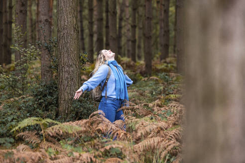 Glückliche junge Frau steht mit ausgestreckten Armen im Cannock Chase Forest - WPEF08091