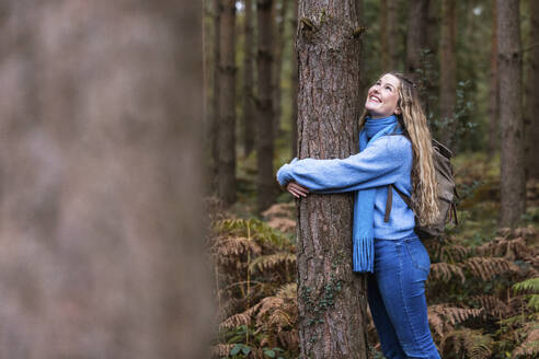 Lächelnde schöne Frau, die einen Baum im Cannock Chase Forest umarmt - WPEF08092