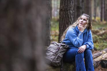 Nachdenkliche Frau sitzt mit Rucksack auf einem Baumstamm im Cannock Chase Forest - WPEF08102