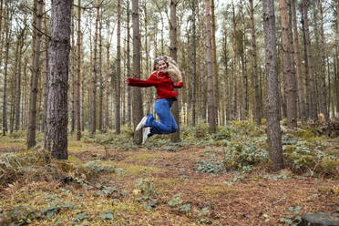 Cheerful woman jumping near trees in Cannock chase forest - WPEF08107