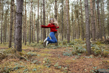 Fröhliche Frau springt in der Nähe von Bäumen im Cannock Chase Forest - WPEF08107