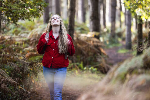 Lächelnde junge Frau beim Spaziergang in der Nähe von Pflanzen im Cannock Chase Forest - WPEF08122