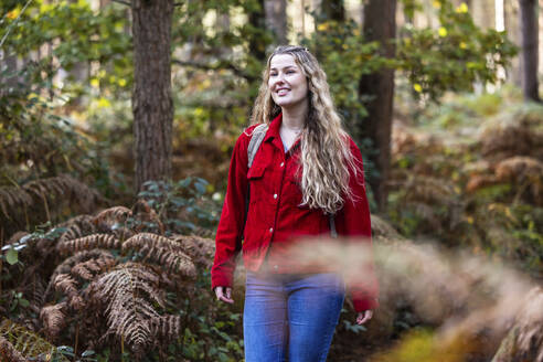 Glückliche junge Frau steht in der Nähe von Pflanzen im Cannock Chase Forest - WPEF08123