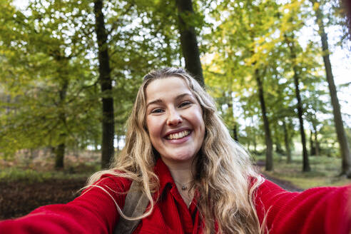 Happy blond woman taking selfie in Cannock chase forest - WPEF08124