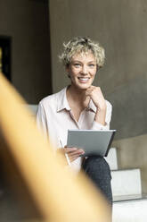 Lächelnde Geschäftsfrau mit Tablet-PC auf den Stufen eines Büros sitzend - PESF04175