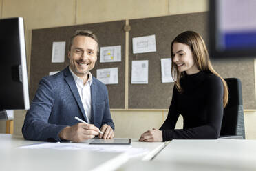 Smiling businessman with tablet PC on desk by trainee in office - PESF04191