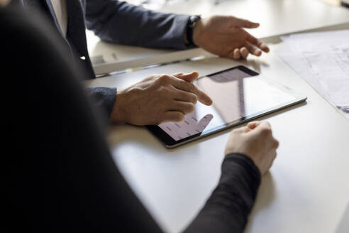 Hand of businessman using tablet computer by colleague at desk in workplace - PESF04198