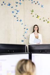 Junge Geschäftsfrau vor einer Wand mit Schmetterlingsaufkleber im Büro - PESF04226
