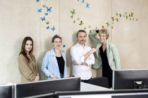 Kollegen stehen vor einer Wand mit Schmetterlingsaufklebern im Büro - PESF04233