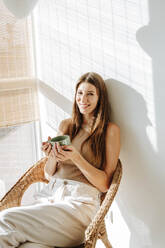 Porträt einer glücklichen Frau mit Kaffeetasse, die sich im Stuhl entspannt - WESTF25294