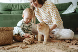 Mother and son with cat playing in the living room at home - WESTF25299