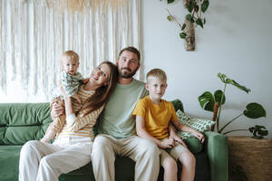 Porträt einer Familie mit zwei Söhnen auf der Couch im Wohnzimmer - WESTF25305