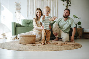 Mother and father playing with their son in living room at home - WESTF25308