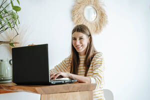 Porträt einer lächelnden Frau, die zu Hause einen Laptop benutzt - WESTF25312