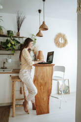 Woman using laptop in kitchen at home - WESTF25315