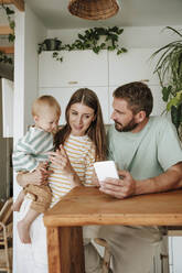 Familie mit kleinem Sohn, der zu Hause auf sein Mobiltelefon schaut - WESTF25330