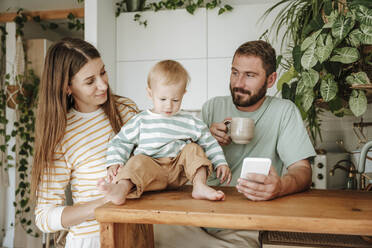 Familie mit kleinem Sohn, der zu Hause auf sein Mobiltelefon schaut - WESTF25331