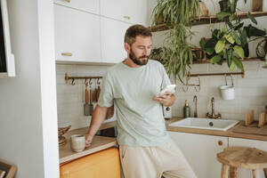 Mann benutzt Mobiltelefon in der Küche zu Hause - WESTF25334