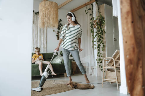 Mother vacuuming the living room and listening to music with headphones at home - WESTF25336