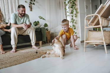 Father watching his son playing with a cat in the living room at home - WESTF25340