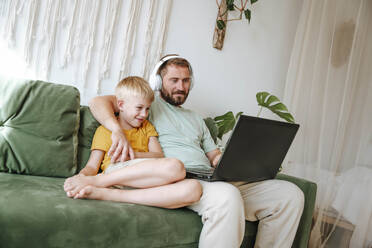 Father and son looking at a laptop while sitting on the couch at home - WESTF25345