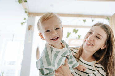 Mother carrying happy son at home - WESTF25349