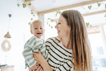 Mother carrying happy son at home - WESTF25350