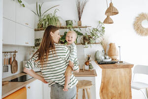 Mother carrying son in kitchen at home - WESTF25351